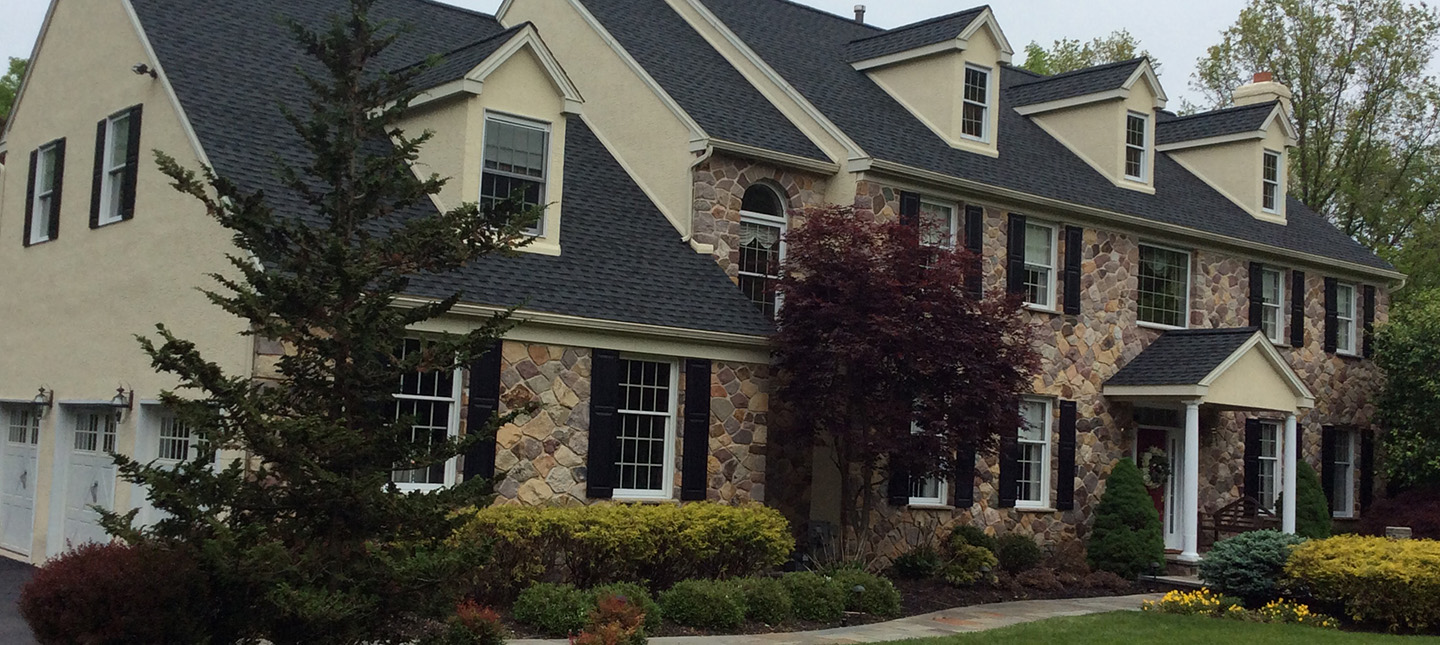 black asphalt shingle roofing on large residential home with tan and stone siding