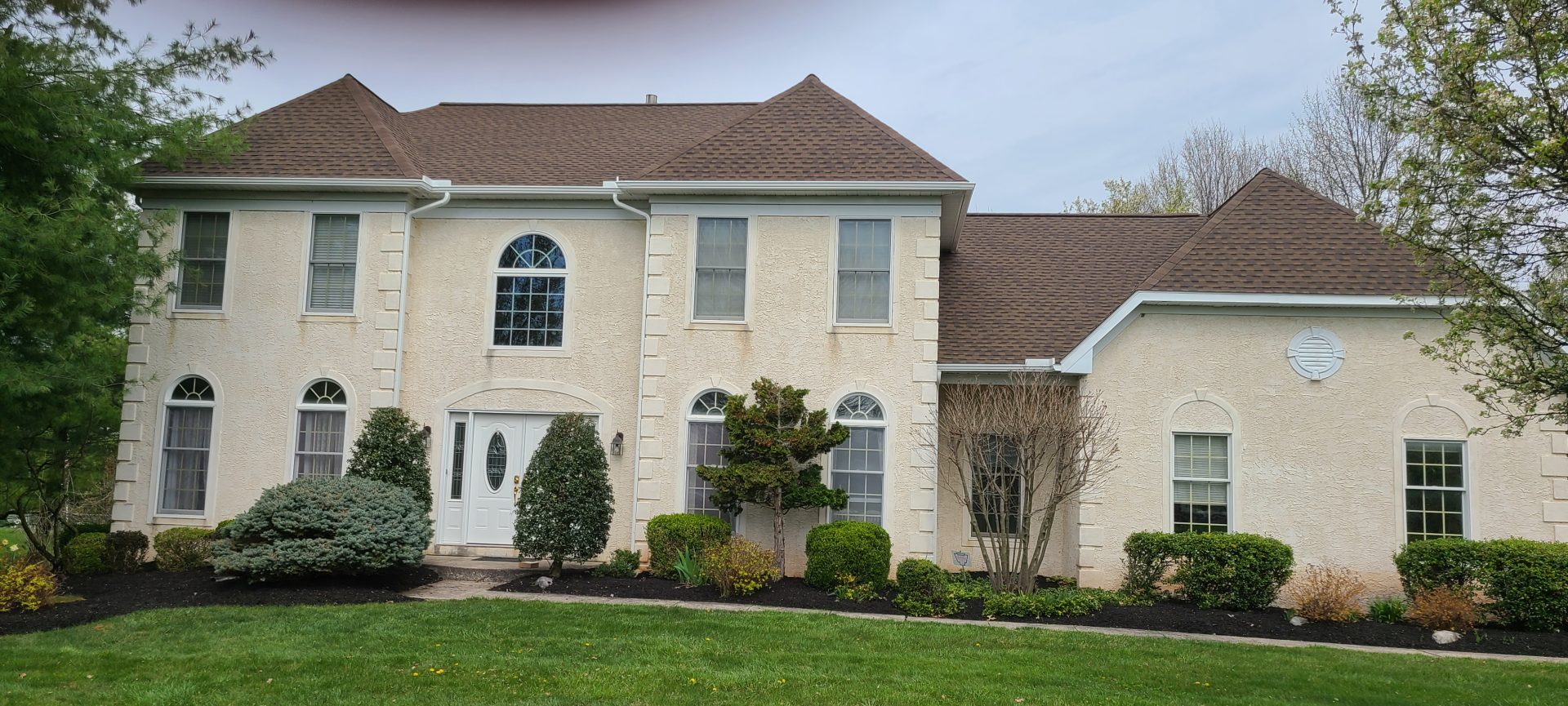 large multiple story residential home featuring tan siding and brown asphalt shingle roofing