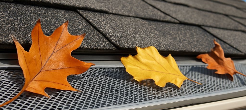 a gray residential home gutter guard blocking three leaves for clogging the gutter